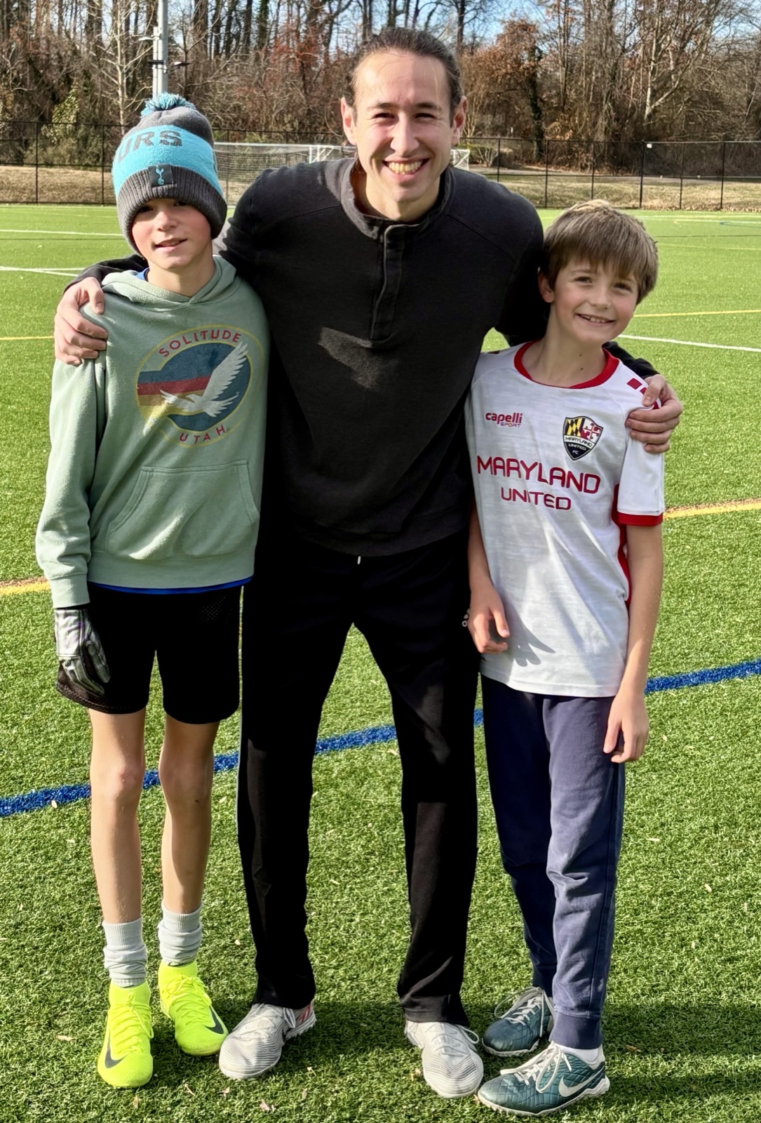 Coach Sam with two young players on the turf field after a session