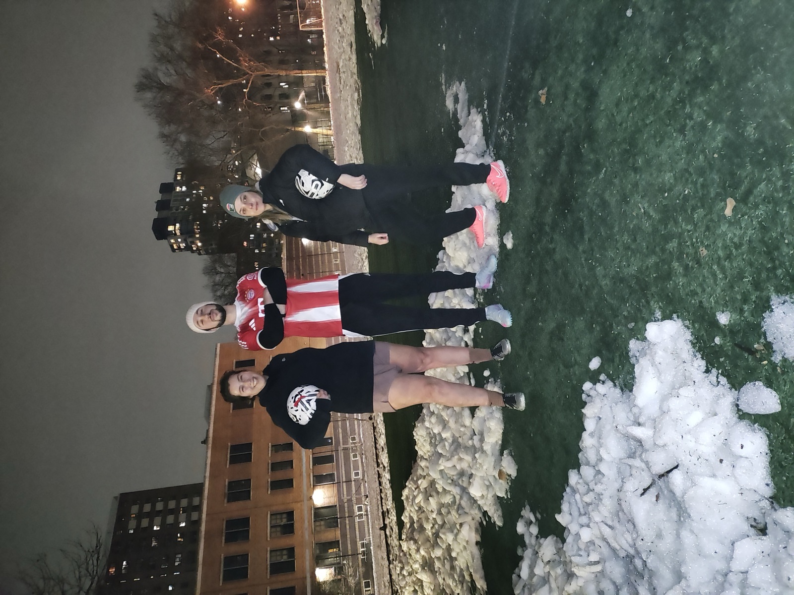 Three coaches posing with soccer balls on a snowy turf field at night