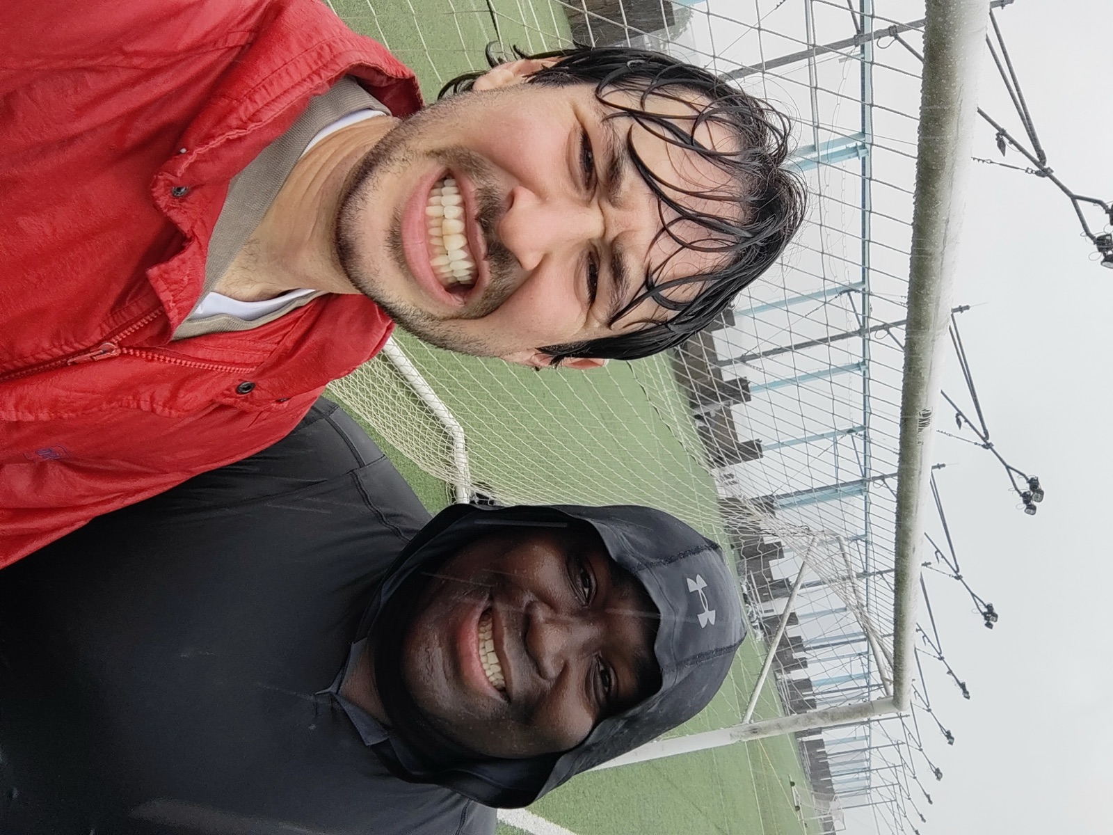 Coach Sam and a fellow coach smiling after a rainy session on the field